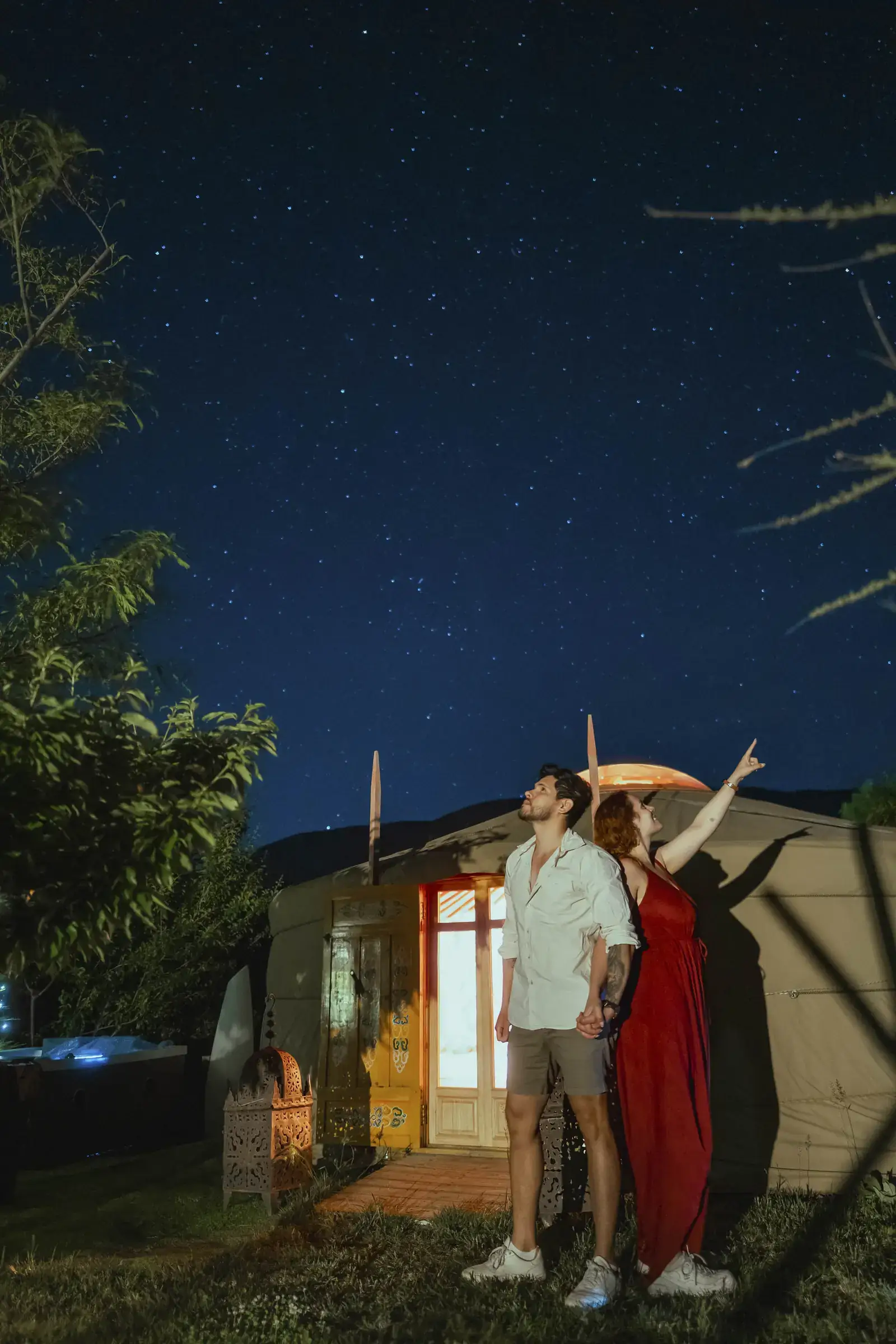 Una pareja mira las estrellas frente a la yurta iluminada, bajo el cielo limpio del Valle del Jerte
